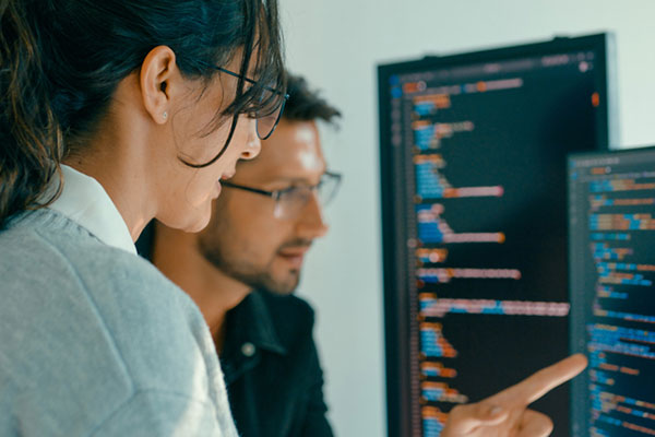 Close-up view of two software engineers in an office examining computer screens with lines of code.