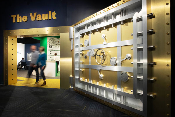 Two people walk through a replica vault door at St. Louis Fed Economy Museum