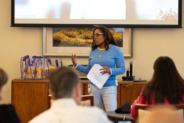 A woman in business attire is standing and speaking to a group that is seated.