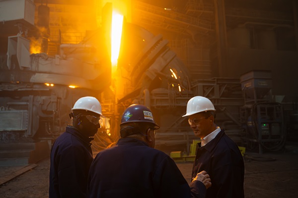 Musalem and two other men wear hardhats and other safety gear at a steel mill.