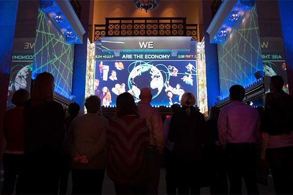 A group of people look at a light show in a large room.