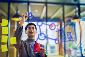 Asian man writing on glass workboard