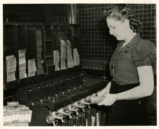 A woman stands in front of a counting machine in the 1940s.