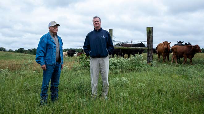 Robert Martinez and Robert Hopkins stand near cattle on a farm.