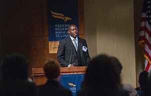 Andre Alexander stands behind a podium with a blue St. Louis Fed banner behind him.