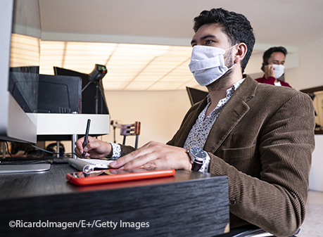 man sitting in front of computer wearing protective mask