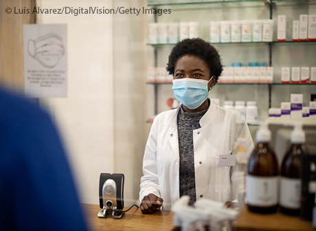 Chemist in face mask assisting costumer at the checkout counter