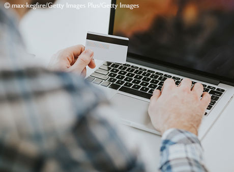 Rear view of male hands holding credit card typing on laptop computer keyboard.