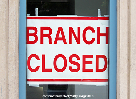 A sign in the window of a bank announces that the branch has closed.