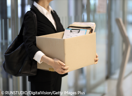 A laid-off employee leaves the office with a cardboard box of personal items.