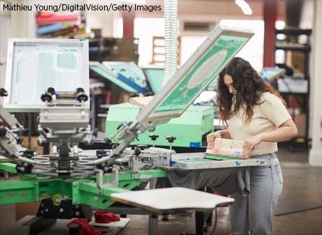 Woman uses screen printer to make custom T-shirts.