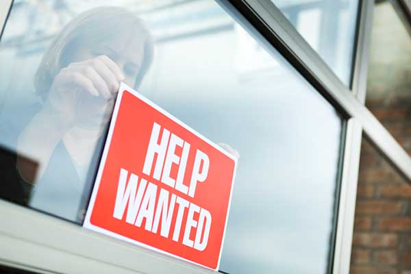 An employee puts up a ‘help wanted’ sign in a store window.