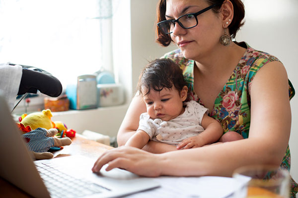 A mom works on a laptop with a baby in her lap.