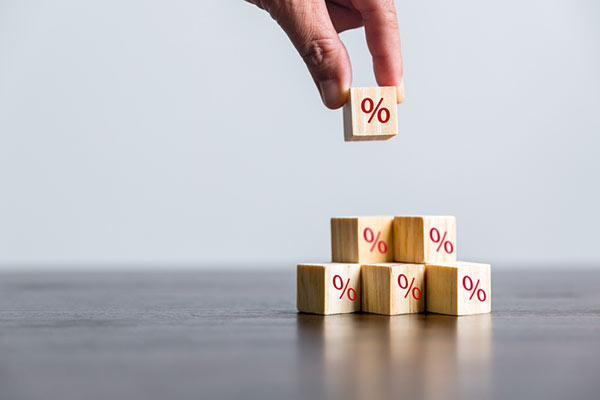 Close-up of hand stacking wooden blocks embossed with the percent sign in red lettering
