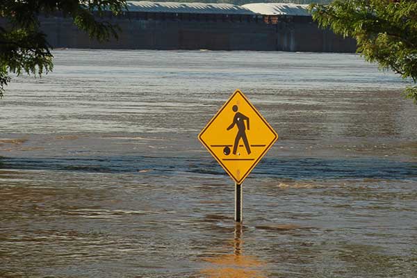 Pedestrian in crosswalk sign in floodwater.