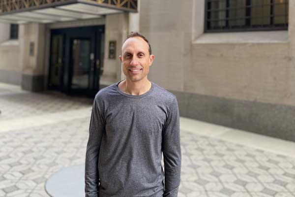 Man in running gear stands in a plaza in front of a stone building.