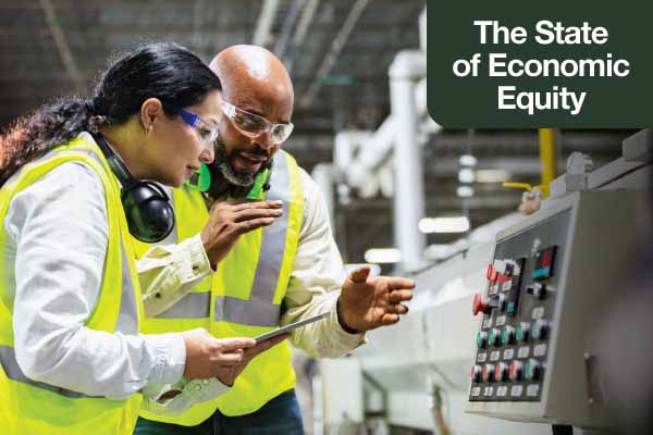 Standing on the floor of a plastics factory, two workers examine the control panel of a machine.