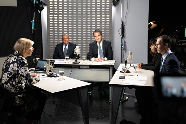 Two women and three men at three tables in a television studio.