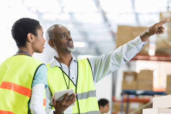 A supervisor gives an orientation briefing to a new employee at a warehouse distribution facility.