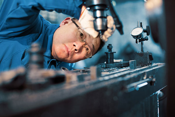 A factory worker examines the bit on a drill press.