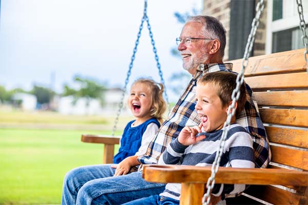 A grandparent sits with two young children on a porch swing.