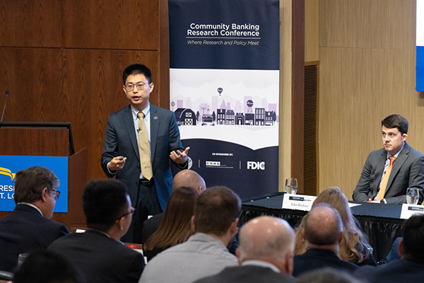 A man in business attire speaks in front of a crowd in an auditorium.