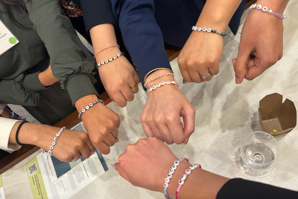 Seven women hold out their wrists to show beaded bracelets.