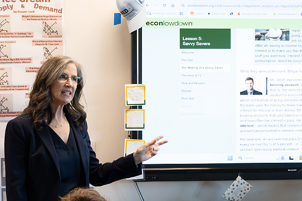 A woman in business attire gestures at a screen showing Econ Lowdown resources.