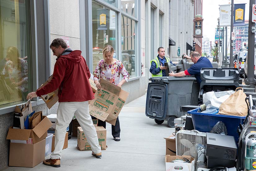 A group of people organize recyclable goods into piles on a sidewalk.