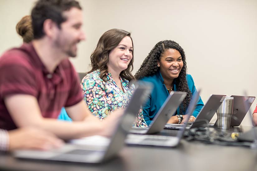 Two women and a man with laptops sit at a table and smile