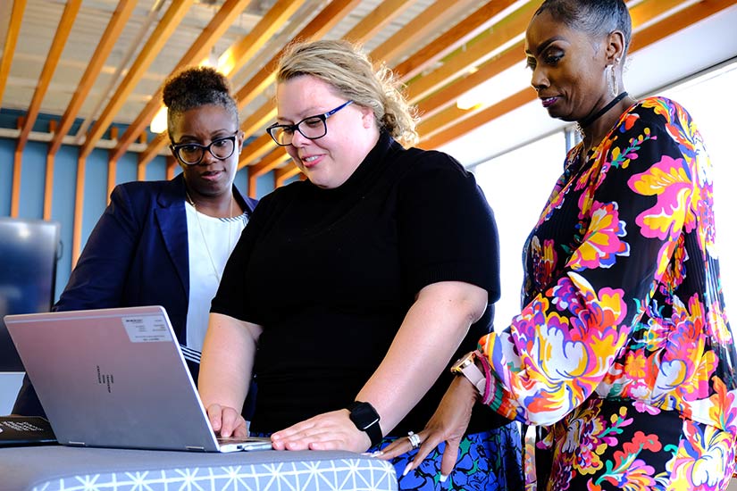 Three women work in front of a laptop computer.