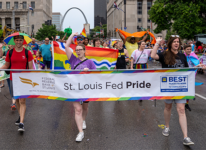 St. Louis Fed employees hold a banner with the text 'St. Louis Fed Pride.' Several individuals hold rainbow-colored flags.