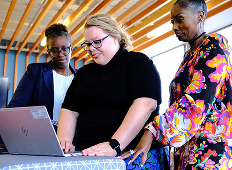 Three women standing by a computer smiling
