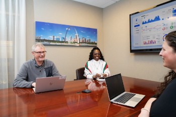 Three people meet around a conference table.