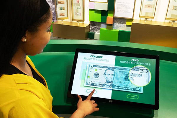Woman touches screen that has an image of the $5 bill.