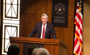 Jerome Powell stands in front of a podium in an auditorium.