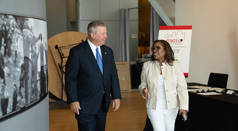 Man and woman walk in foyer next to welcome table at an event.