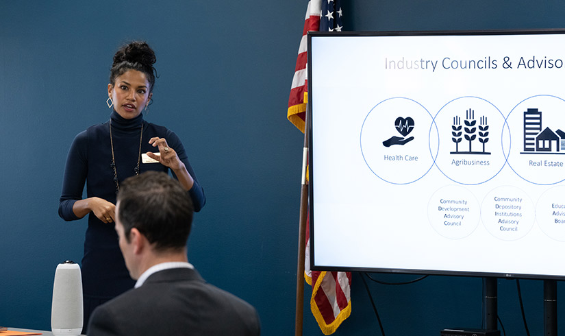 Seema Sheth stands at the front of a room, presenting to an audience.
