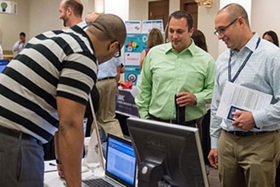 three men gather around a laptop