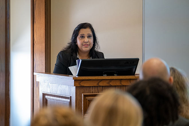 Woman in black blazer stands at podium