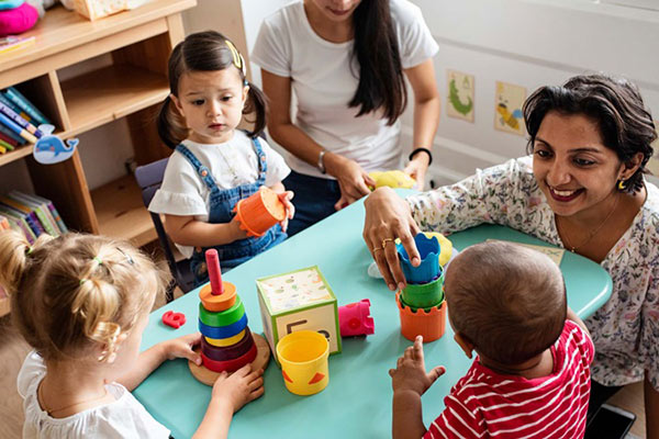 Daycare providers and children play with toys at a table