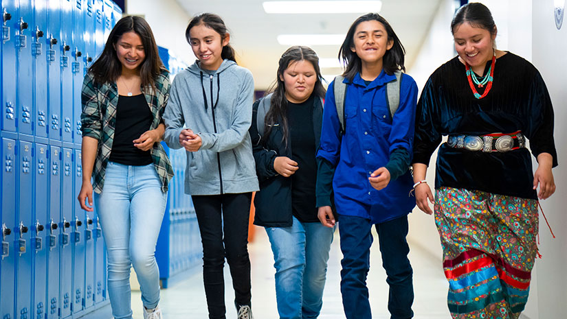 A group of young students walks through a school hallway lined with lockers.