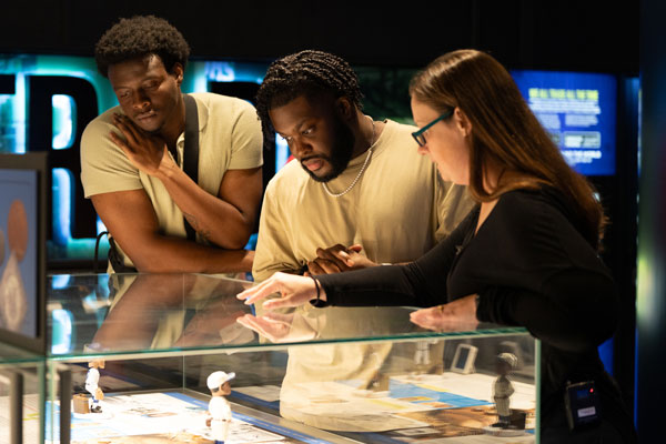 Two men and a woman stand over a museum exhibit.