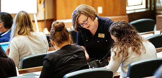 Educator in a lecture hall, assisting two high school students