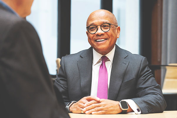 Man in a suit smiles at someone sitting across the table from him.