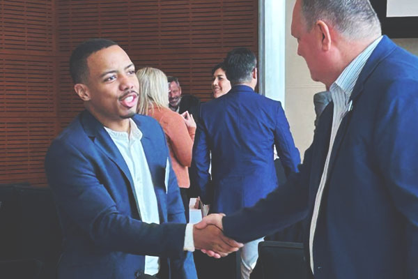 Two men in suits converse as they shake hands.
