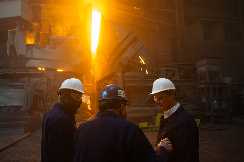 Musalem and two other men wear hardhats and other safety gear at a steel mill.