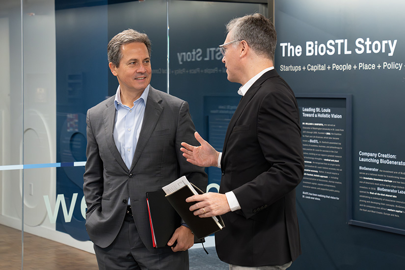 A man speaks with Musalem in front of glass doors and a wall with 'The BioSTL Story' text.