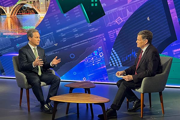 Two men dressed in business attire seated in a studio are engaged in conversation.