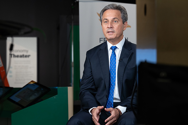 A man dressed in business attire is seated and speaking.